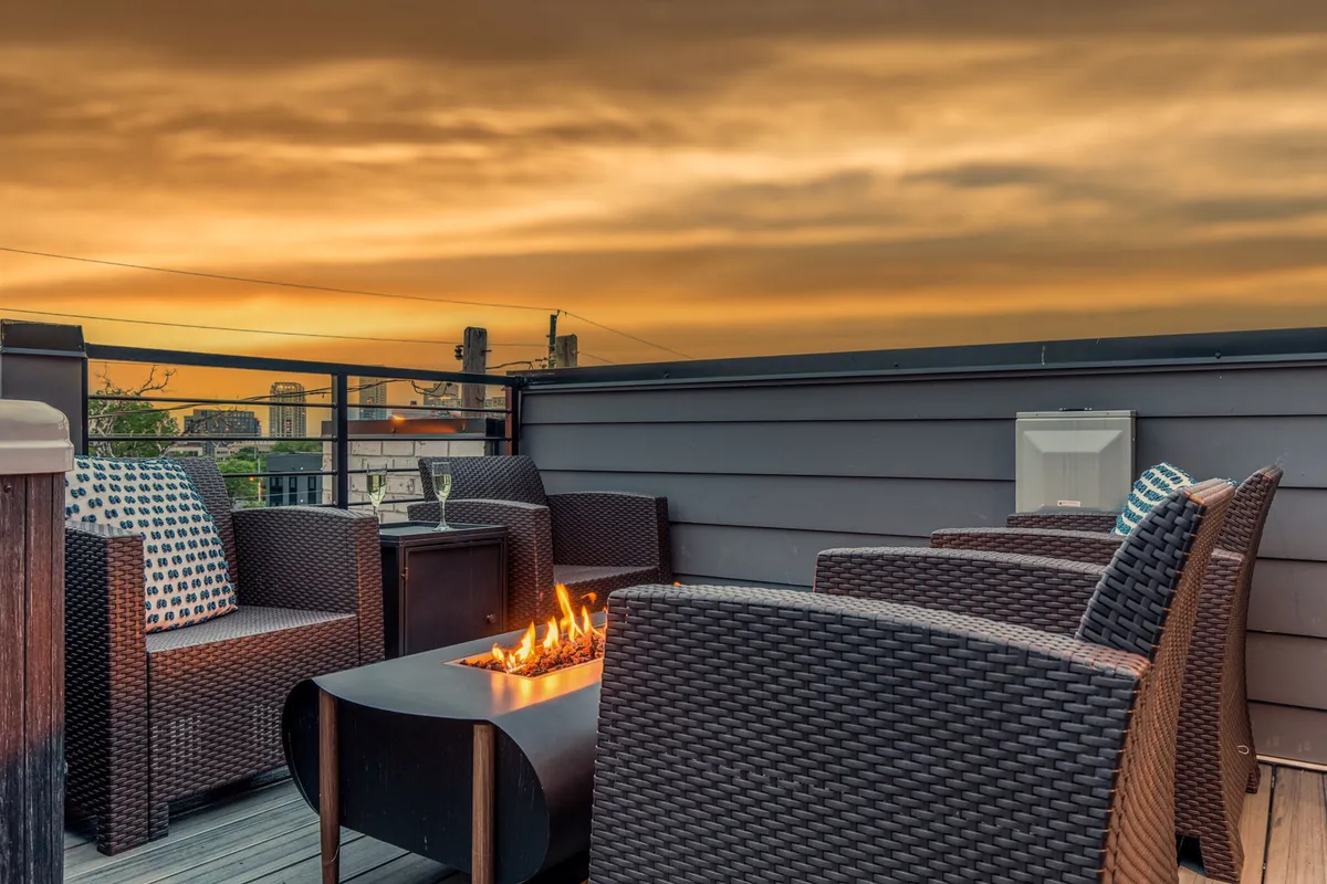 A cozy outdoor fire pit area with comfortable wicker chairs arranged for conversation, all set against a colorful sunset sky. The scene exudes intimacy and warmth, inviting groups to gather, socialize, or enjoy stargazing and relaxed evenings together.
