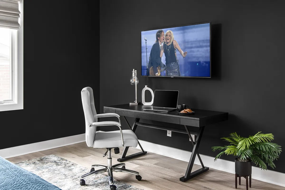 A bedroom workspace setup with a modern desk, flat-screen TV, and a potted plant. The environment is comfortable and contemporary, ideal for guests who need to work or unwind with entertainment options at hand.