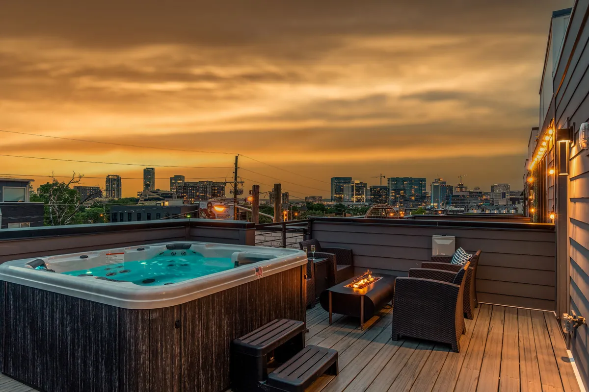 A stunning private rooftop setting featuring a hot tub, stylish outdoor seating, ambient string lighting, and sweeping views of the Nashville city skyline at sunset. The space is designed for relaxation and social gatherings, inviting guests to unwind or celebrate in luxury while connected to the city’s vibrant energy.