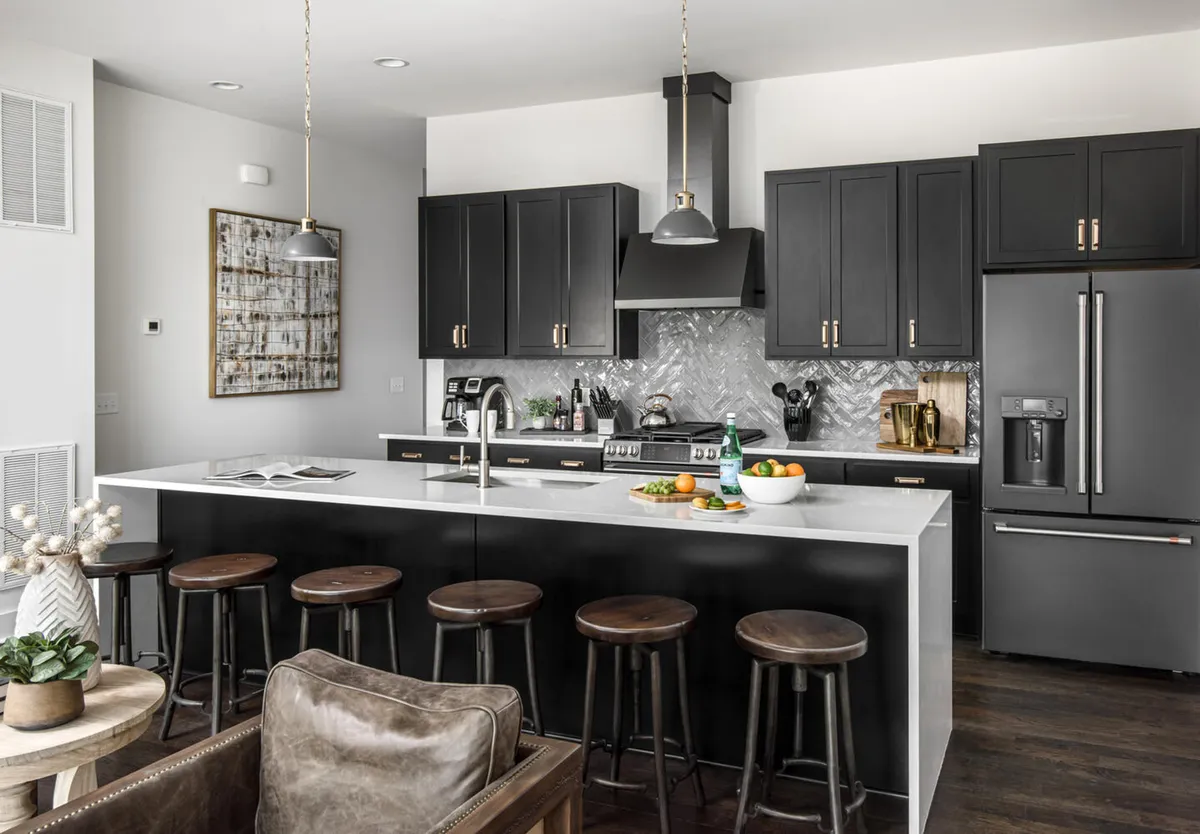 A contemporary kitchen island with a fruit bowl centerpiece, surrounded by stools and set against a backdrop of modern black cabinetry. The space feels open and welcoming, perfect for gathering during meal prep or casual dining.