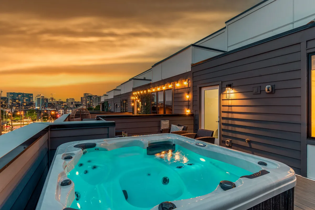 A luxurious rooftop scene featuring a private hot tub, ambient lighting, and the Nashville city skyline in the background. The tranquil atmosphere suggests relaxation above the bustling city, perfect for unwinding or entertaining after a day exploring.