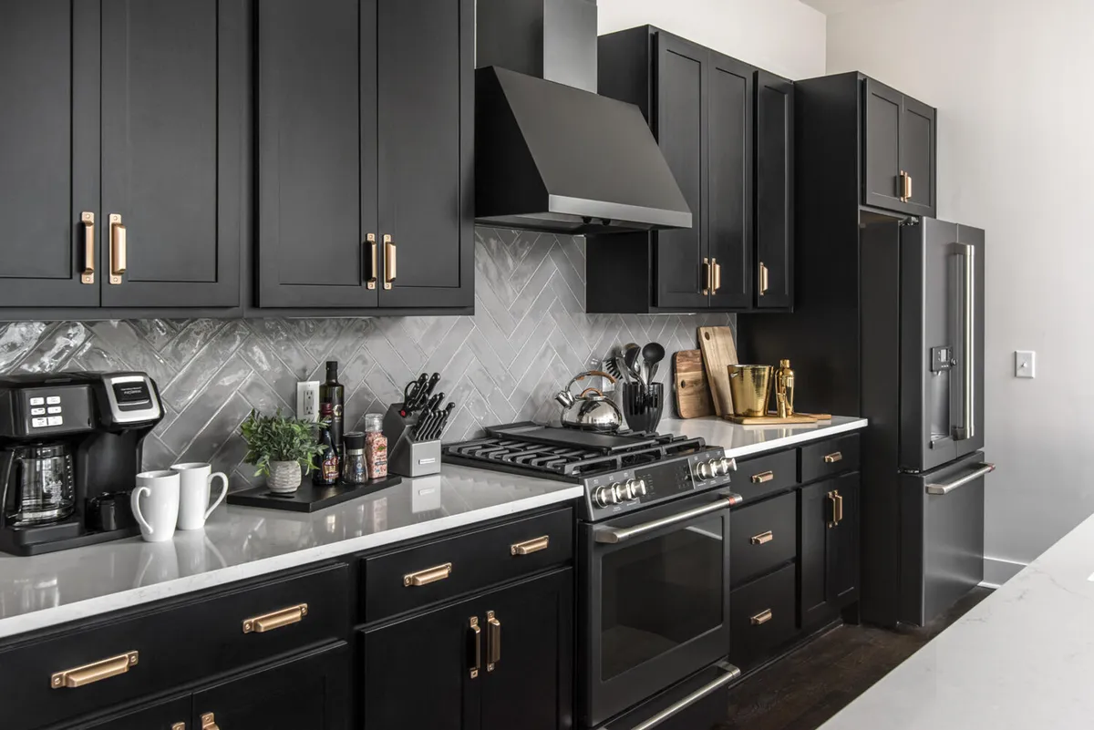 A modern kitchen featuring black cabinetry, stainless steel appliances, a striking herringbone backsplash, and expansive white countertops. The focal point is the oversized island with bar seating, seamlessly integrated for both cooking and socializing.
