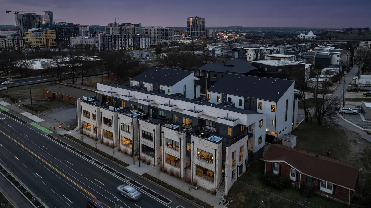 A wide-angle exterior view of the modern townhouses, with the Nashville city skyline visible in the background. The street scene conveys a sense of vibrant urban living and the property's central location, with easy access to city amenities.