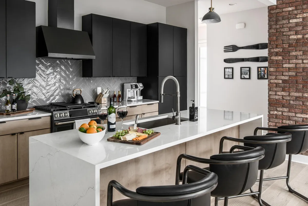 A beautifully styled kitchen with a sleek black island, white countertops, an artfully arranged charcuterie board, and wine glasses ready for a toast. The cabinetry, modern fixtures, and open design emphasize both functionality and style.
