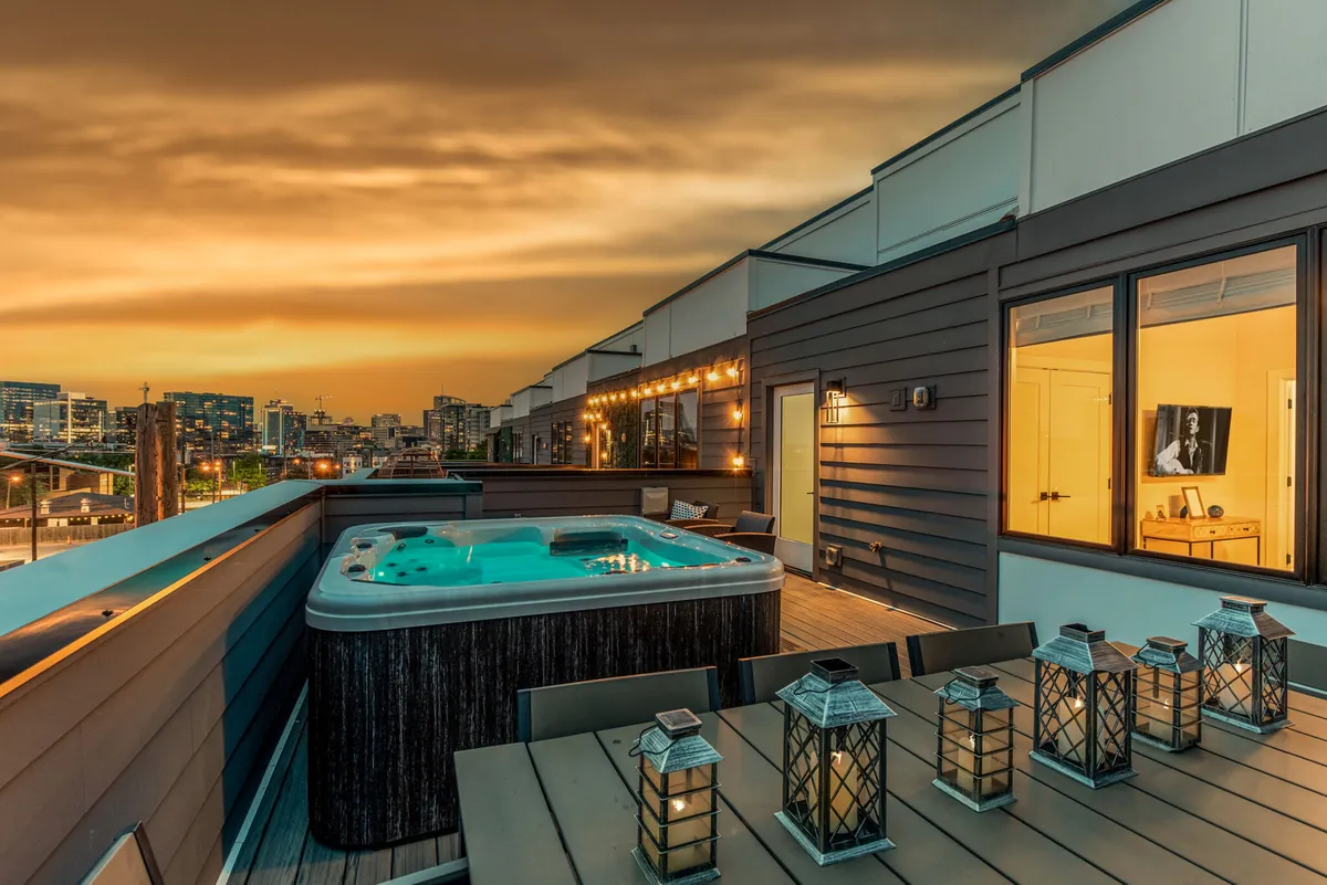 A luxurious rooftop deck view featuring a hot tub, an outdoor dining area, and an impressive city skyline backdrop. The atmosphere is tranquil yet sophisticated, perfect for unwinding after a productive day or hosting informal team gatherings.
